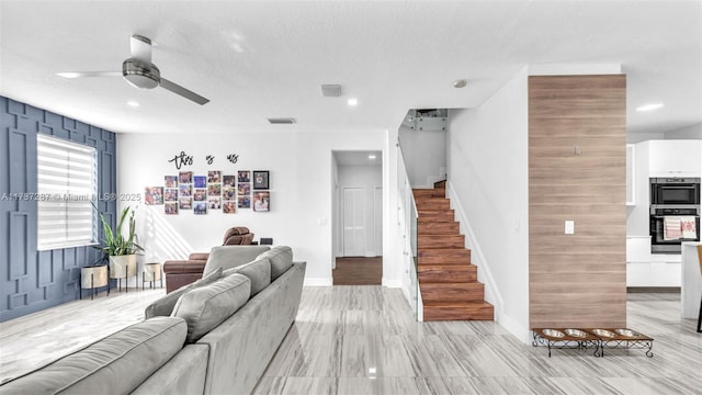 living room featuring a textured ceiling, visible vents, baseboards, stairs, and a ceiling fan