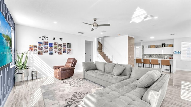 living room with a ceiling fan, visible vents, stairway, and baseboards