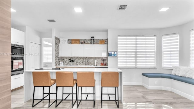 kitchen featuring black appliances, a kitchen bar, light countertops, and white cabinets