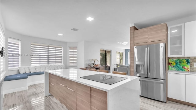 kitchen with modern cabinets, light countertops, stainless steel refrigerator with ice dispenser, and black electric cooktop