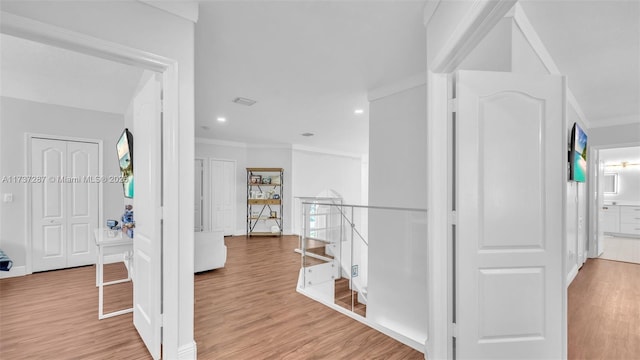 corridor with ornamental molding, light wood-type flooring, and an upstairs landing