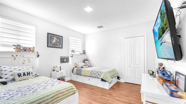 bedroom with light wood finished floors, baseboards, visible vents, and a closet