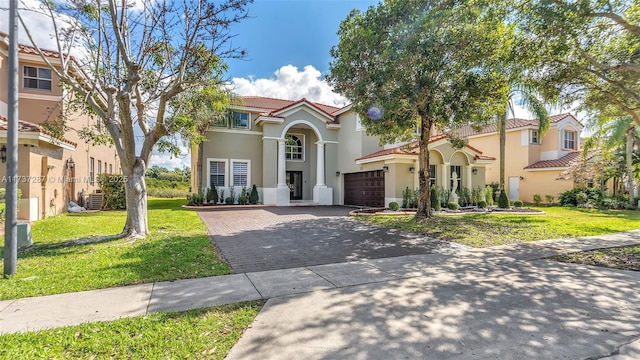 mediterranean / spanish home featuring decorative driveway, a tile roof, a front lawn, and stucco siding