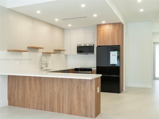 kitchen featuring sink, oven, white cabinets, kitchen peninsula, and black fridge