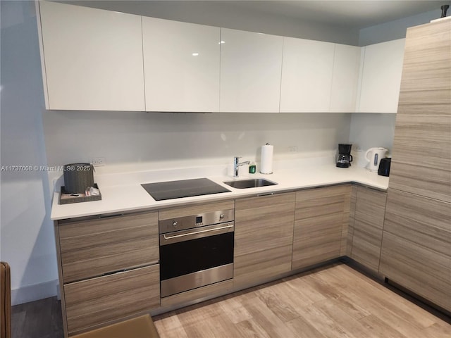 kitchen featuring sink, white cabinets, oven, light hardwood / wood-style floors, and black electric cooktop