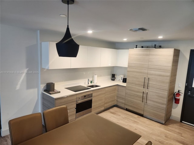 kitchen with decorative light fixtures, white cabinetry, sink, stainless steel oven, and black electric cooktop