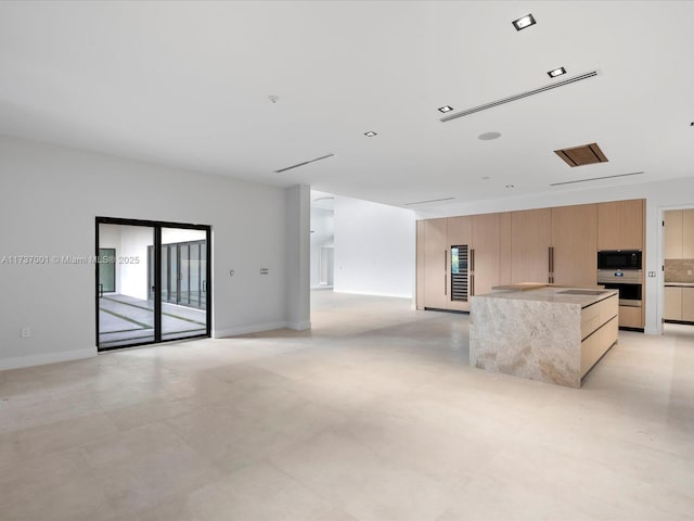 kitchen featuring light brown cabinetry, oven, black microwave, and a kitchen island