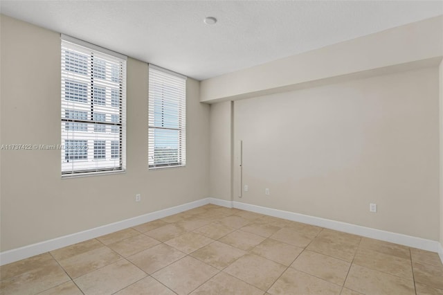 empty room with a textured ceiling, baseboards, and light tile patterned floors