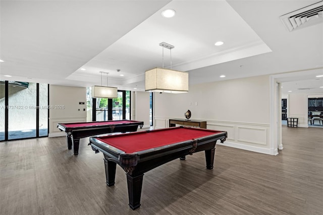 recreation room with a tray ceiling, visible vents, a decorative wall, and wood finished floors