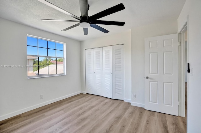 unfurnished bedroom with ceiling fan, a textured ceiling, a closet, and light wood-type flooring