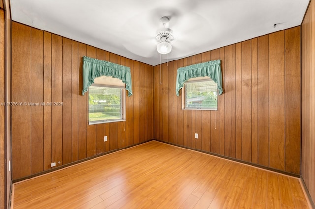 empty room with ceiling fan, a healthy amount of sunlight, wooden walls, and light wood-type flooring