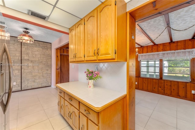 kitchen with light tile patterned flooring, wooden walls, tile counters, and decorative backsplash