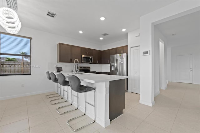 kitchen with light tile patterned flooring, a kitchen bar, kitchen peninsula, stainless steel appliances, and dark brown cabinets