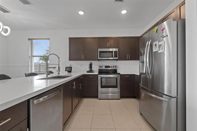 kitchen with sink, decorative light fixtures, dark brown cabinets, light tile patterned floors, and appliances with stainless steel finishes