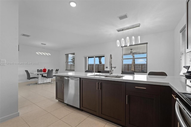 kitchen with sink, light tile patterned floors, appliances with stainless steel finishes, hanging light fixtures, and dark brown cabinets