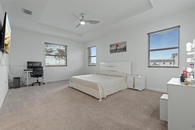 bedroom featuring a raised ceiling, light carpet, and ceiling fan