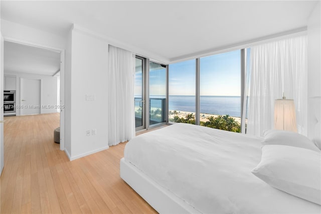 bedroom featuring a water view, access to exterior, and light hardwood / wood-style floors