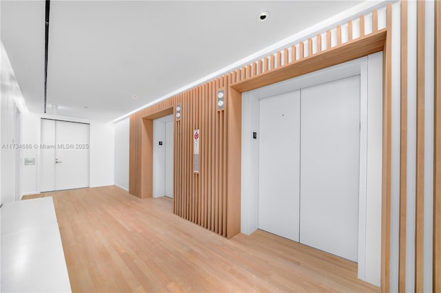 corridor with light hardwood / wood-style floors and elevator