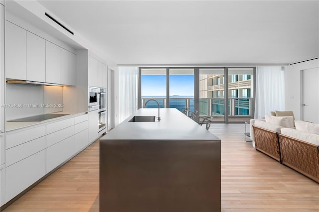 kitchen featuring an island with sink, sink, white cabinets, stainless steel oven, and black electric stovetop