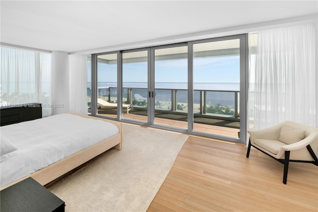 bedroom with hardwood / wood-style floors, access to outside, floor to ceiling windows, and a water view