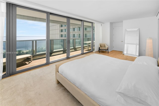 bedroom featuring light wood-type flooring, access to outside, a wall of windows, and a water view