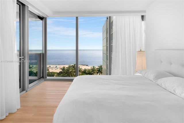 bedroom featuring a water view, multiple windows, a wall of windows, and light hardwood / wood-style flooring