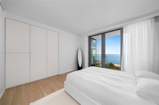 bedroom with a water view, access to outside, light hardwood / wood-style floors, and french doors