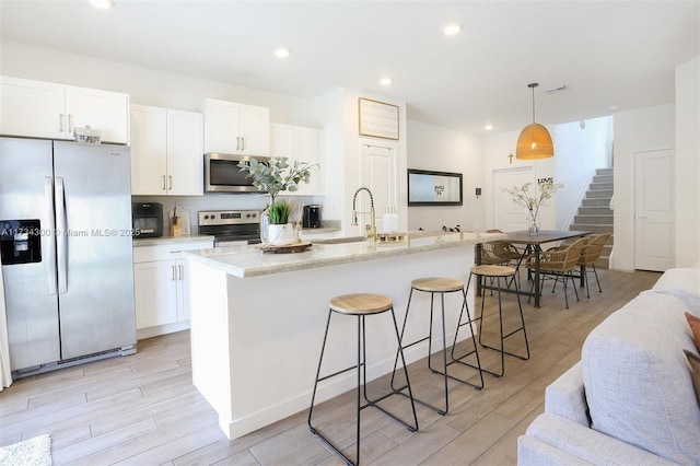 kitchen featuring white cabinetry, stainless steel appliances, a kitchen island with sink, and light stone counters