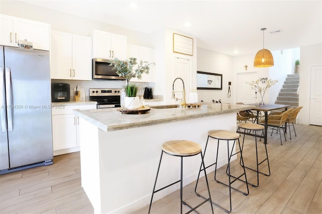 kitchen with white cabinetry, appliances with stainless steel finishes, sink, and a kitchen island with sink