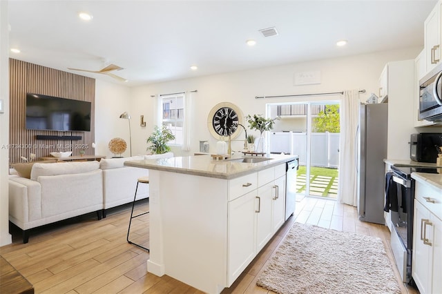 kitchen featuring stainless steel appliances, an island with sink, sink, and white cabinets