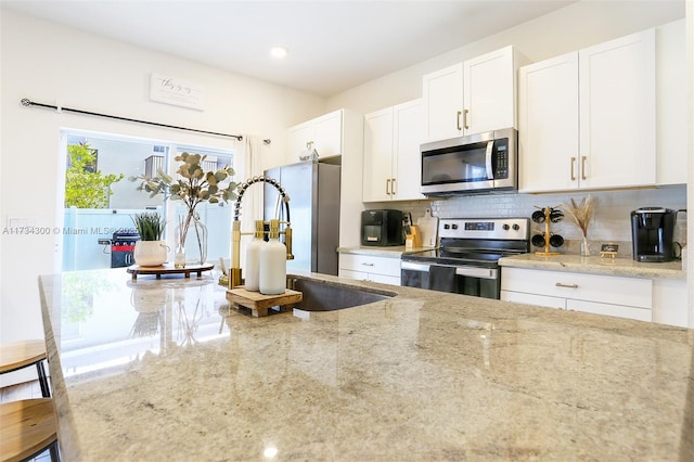 kitchen with light stone countertops, a kitchen breakfast bar, white cabinets, and appliances with stainless steel finishes