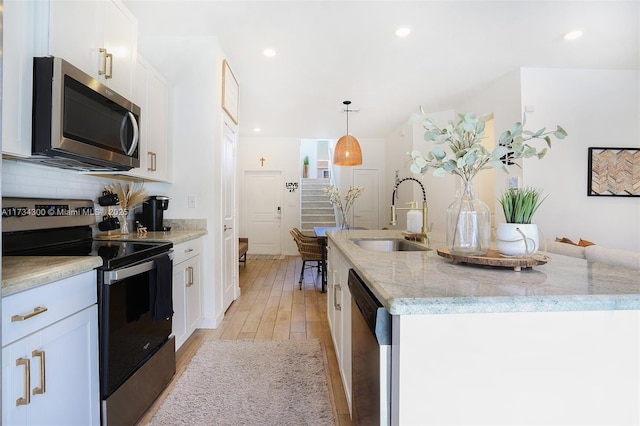 kitchen with pendant lighting, sink, appliances with stainless steel finishes, an island with sink, and white cabinets