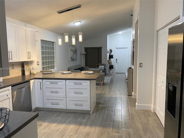 kitchen with white cabinetry, lofted ceiling, hanging light fixtures, kitchen peninsula, and stainless steel appliances