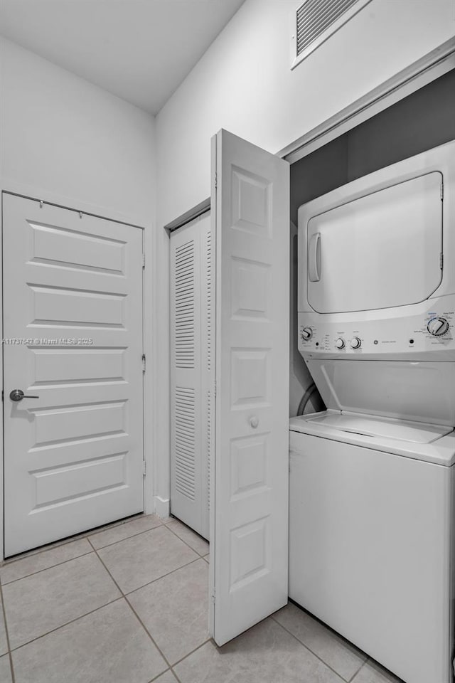 laundry area with stacked washing maching and dryer and light tile patterned floors