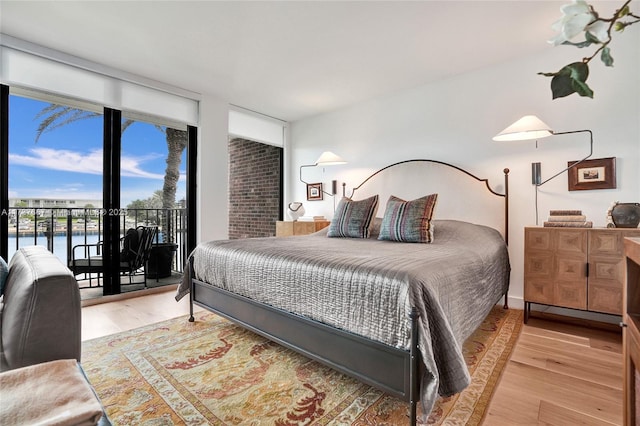 bedroom featuring access to exterior, light hardwood / wood-style flooring, expansive windows, and a water view