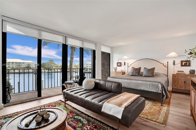 bedroom featuring a water view, access to outside, a wall of windows, and light hardwood / wood-style flooring