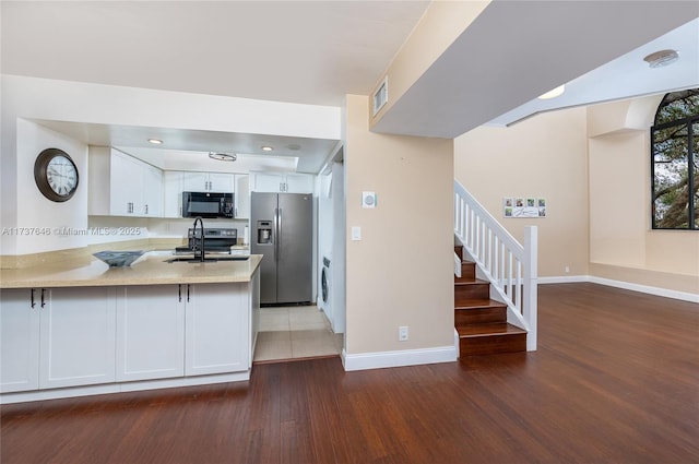 kitchen with sink, appliances with stainless steel finishes, dark hardwood / wood-style flooring, kitchen peninsula, and white cabinets