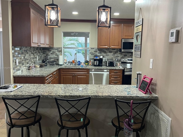 kitchen with pendant lighting, sink, a breakfast bar area, stainless steel appliances, and light stone countertops