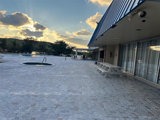 patio terrace at dusk featuring a community pool