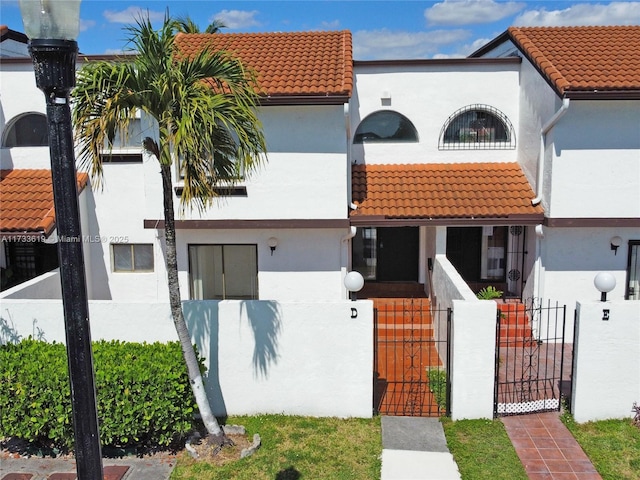 mediterranean / spanish house with a fenced front yard, a gate, a tile roof, and stucco siding