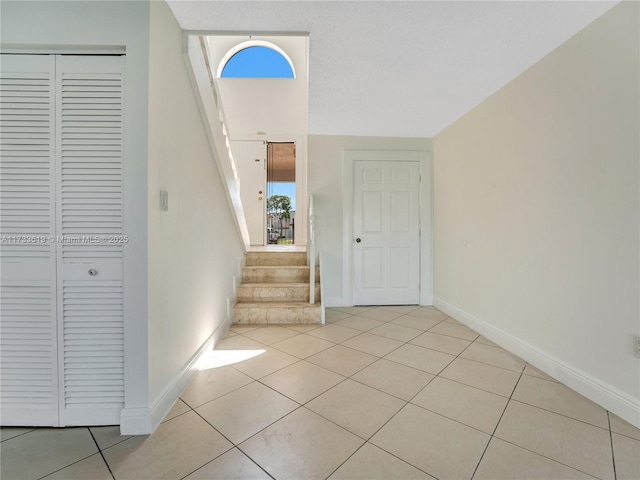 foyer entrance featuring light tile patterned floors, stairway, and baseboards