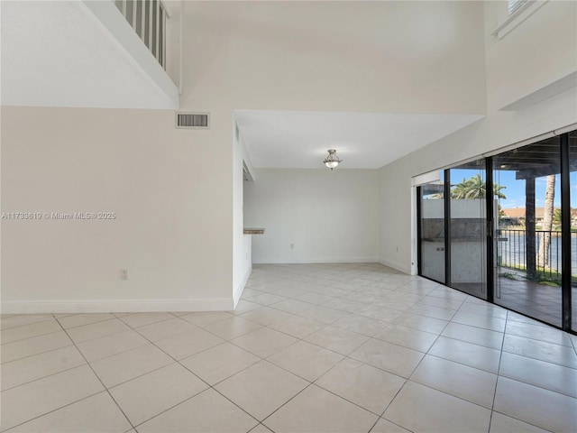 unfurnished room featuring a towering ceiling, light tile patterned floors, baseboards, and visible vents