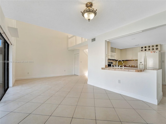 unfurnished living room with light tile patterned floors, visible vents, a sink, a textured ceiling, and baseboards