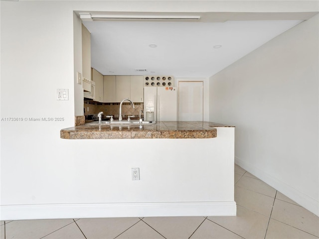 kitchen with tile countertops, decorative backsplash, cream cabinets, a sink, and white fridge with ice dispenser