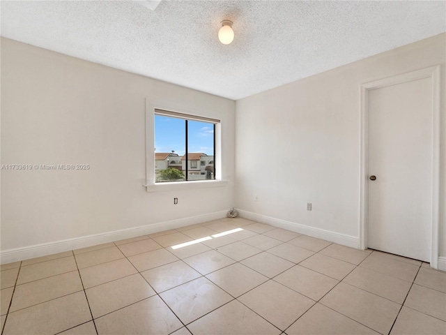 spare room featuring light tile patterned floors, a textured ceiling, and baseboards