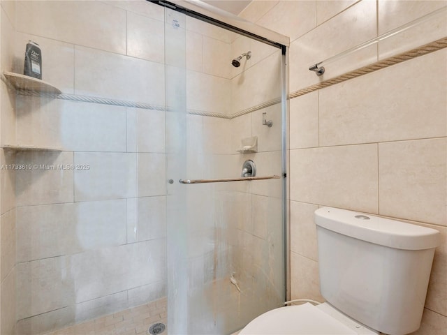 bathroom featuring toilet, a shower stall, and tile walls