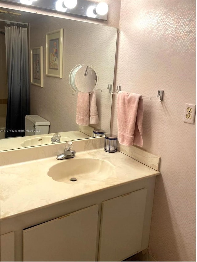 bathroom featuring toilet, a textured wall, curtained shower, and vanity