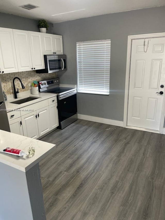 kitchen featuring appliances with stainless steel finishes, white cabinetry, sink, backsplash, and dark wood-type flooring