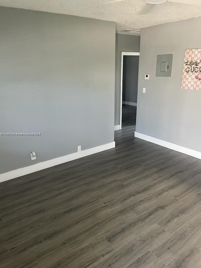 empty room featuring dark wood-type flooring, electric panel, and a textured ceiling