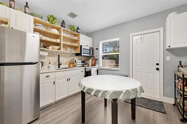 kitchen featuring white cabinetry, sink, light hardwood / wood-style floors, and appliances with stainless steel finishes